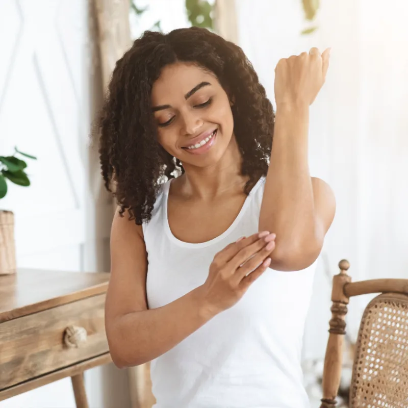 Woman smiling applying skin medication on her elbow.